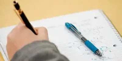 A close up of a hand writing math in a notebook